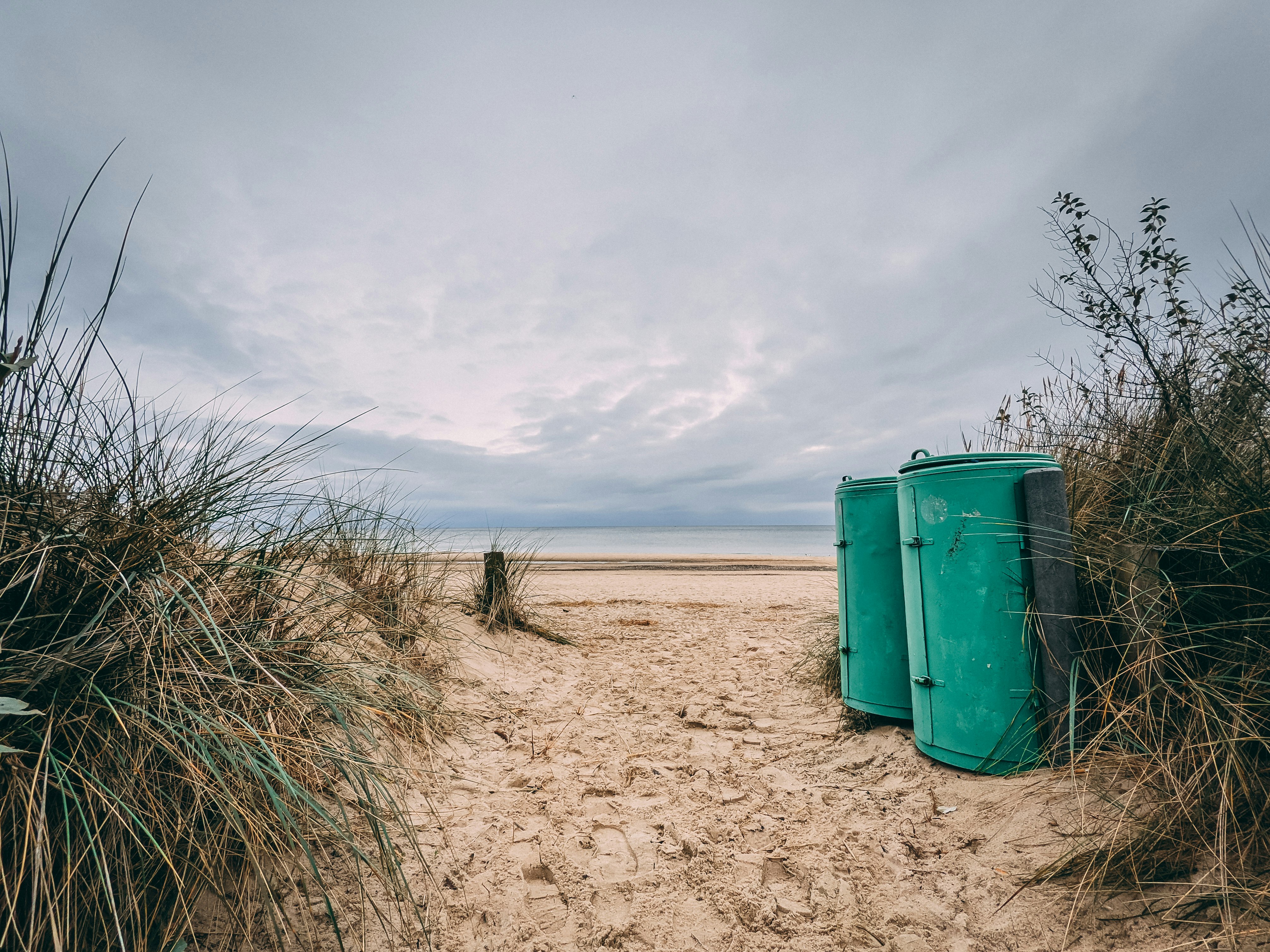 green trash bin on brown sand under white clouds during daytime